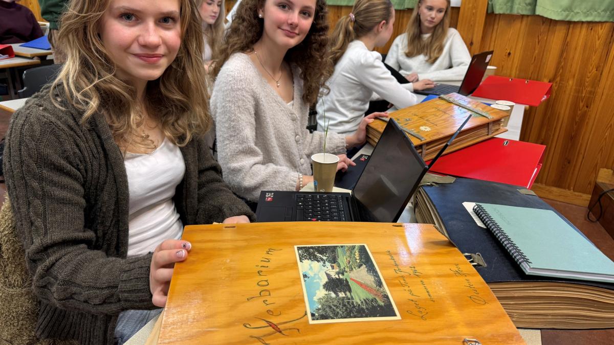 To jente-elever sitter i klasserommet og kikker på et gammelt herbarium.