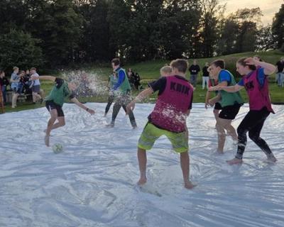 Elever spiller fotball på en presenningsmatte full av såpe