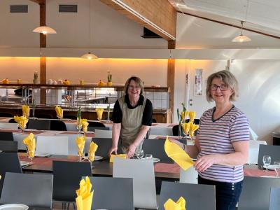 To damer dekker til i matsalen, pynter med gule servietter