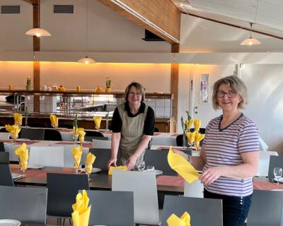 To damer dekker til i matsalen, pynter med gule servietter
