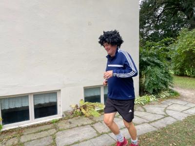 Mann som løper i idrettsklær og med sort parykk.