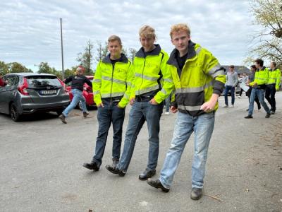 3 elever står oppstilt i gule arbeidsjakker og dongri.