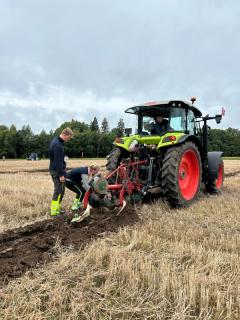 Pløying på et jorde. En traktor med pløyeredskap.