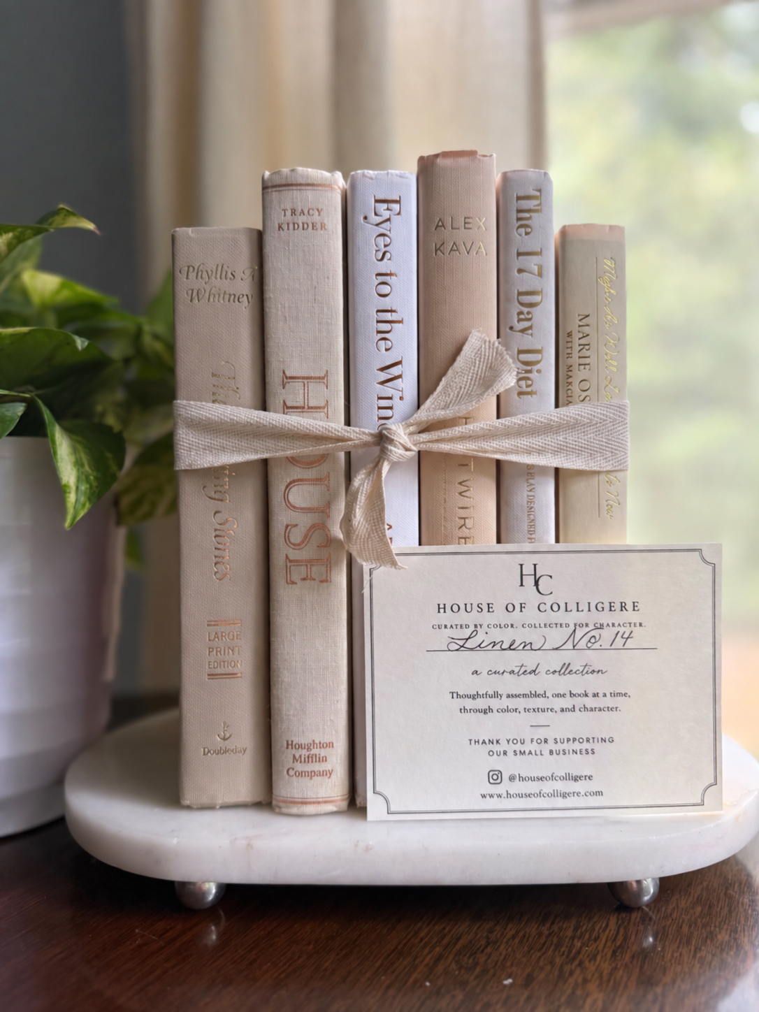 Six white, ivory, and pale taupe hardcover books tied with natural ribbon on a marble tray, with gold-toned lettering and a Linen No. 10 card.