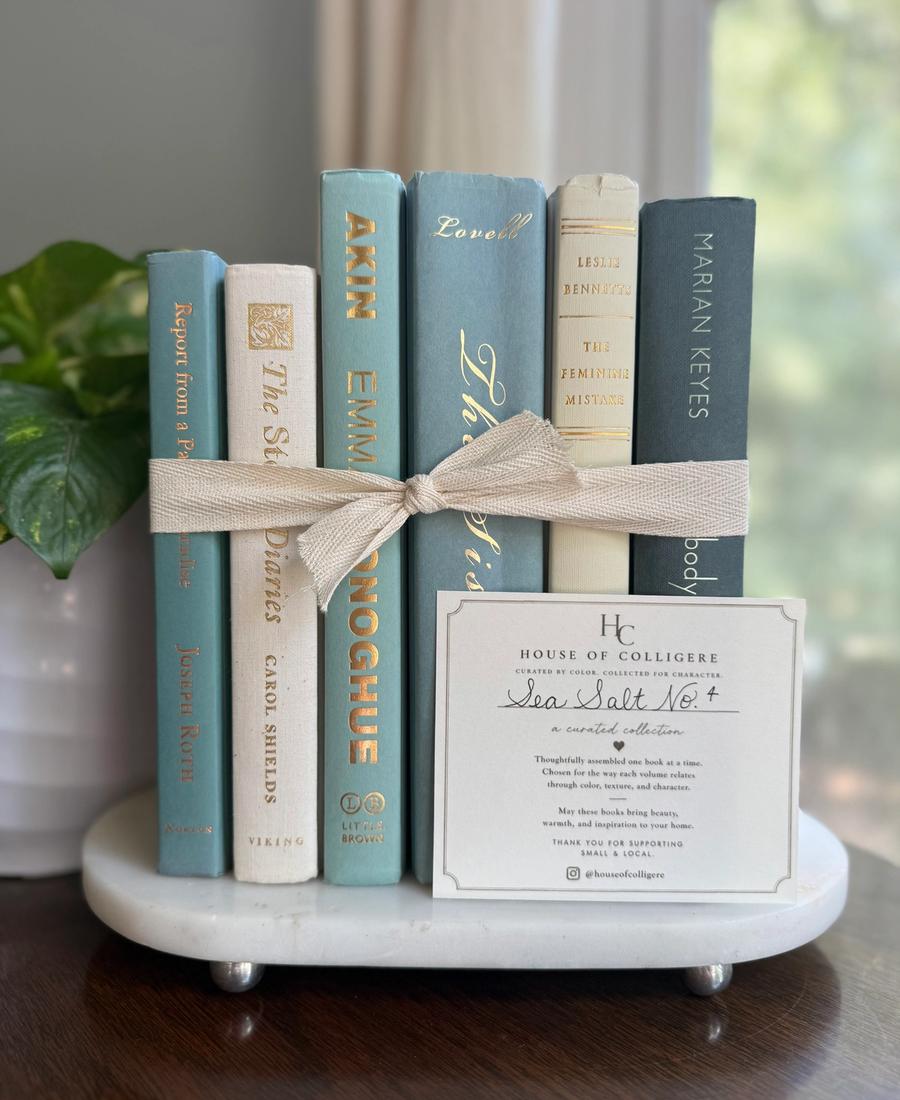 Curated collection of white, pale blue, sand, and soft coastal-neutral books with an airy, sun-faded look.
