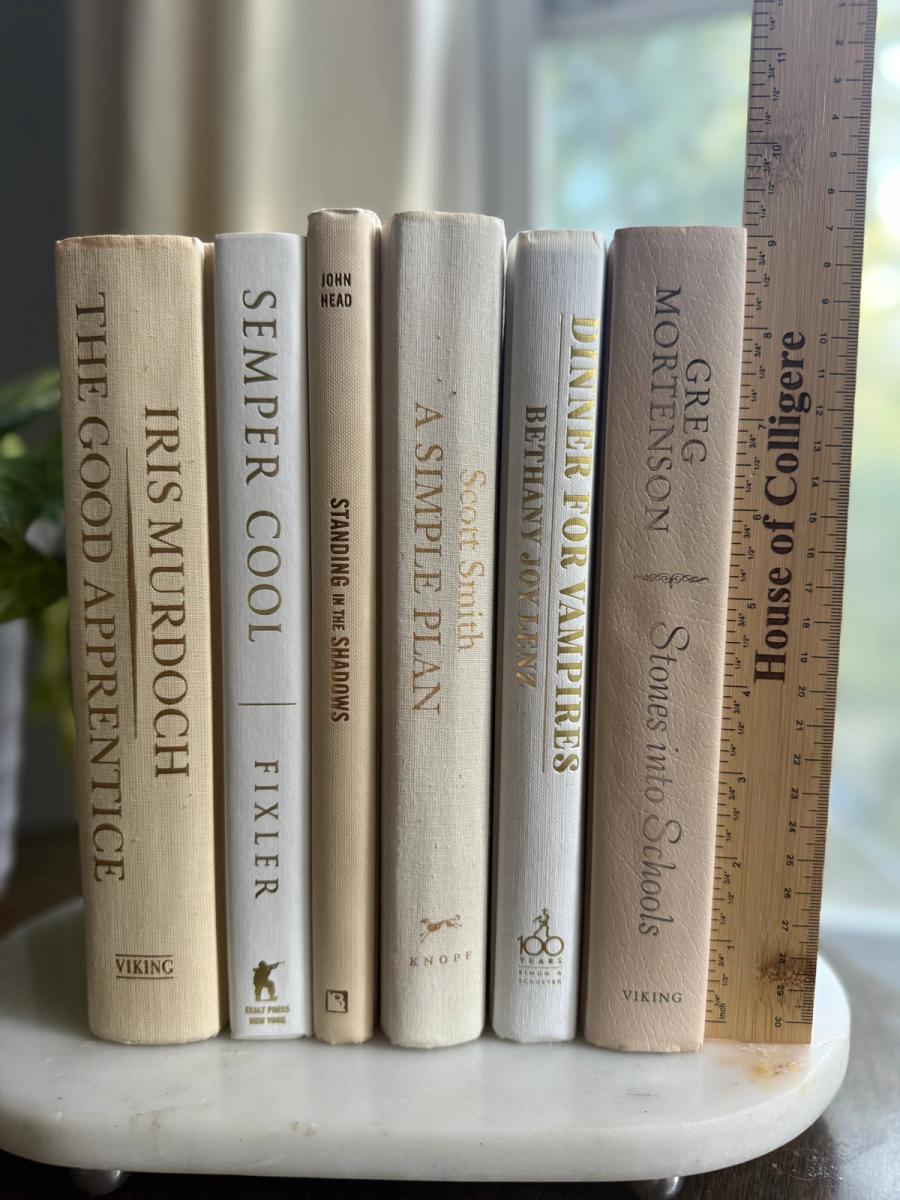 Curated collection of white, ivory, and cream hardcover books with soft neutral tones on a coffee table beside a plant 