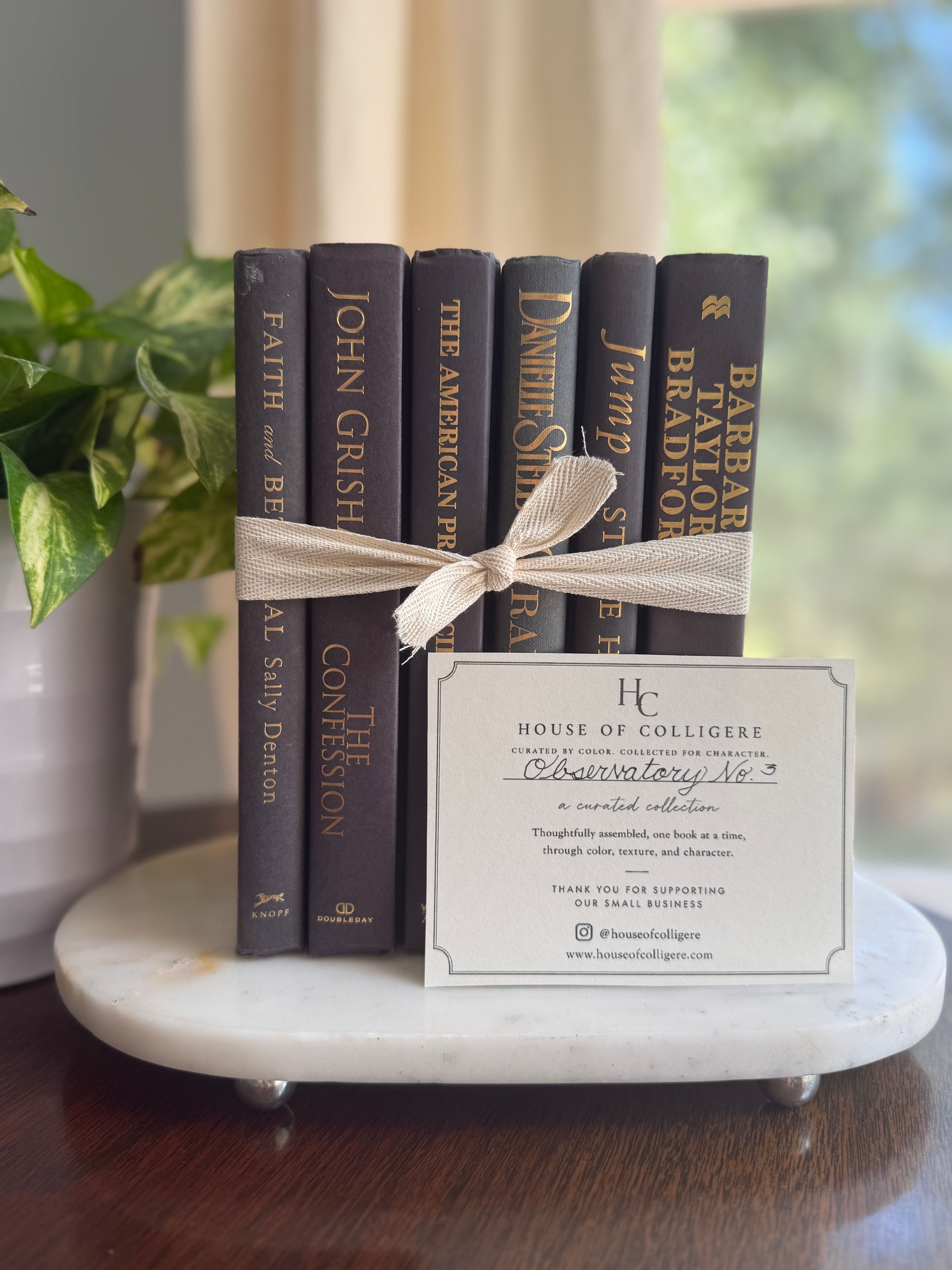 Curated collection of rich charcoal and black books with warm gold lettering and dramatic tonal depth.