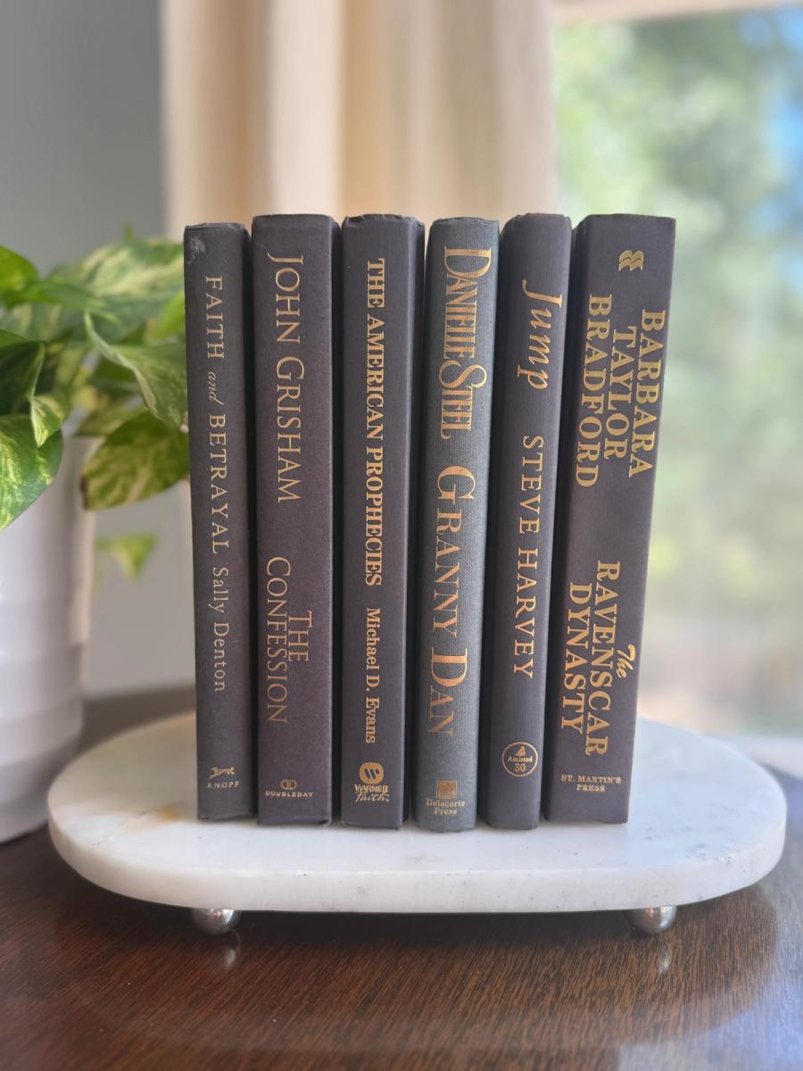 Curated collection of rich charcoal and black books with warm gold lettering and dramatic tonal depth.