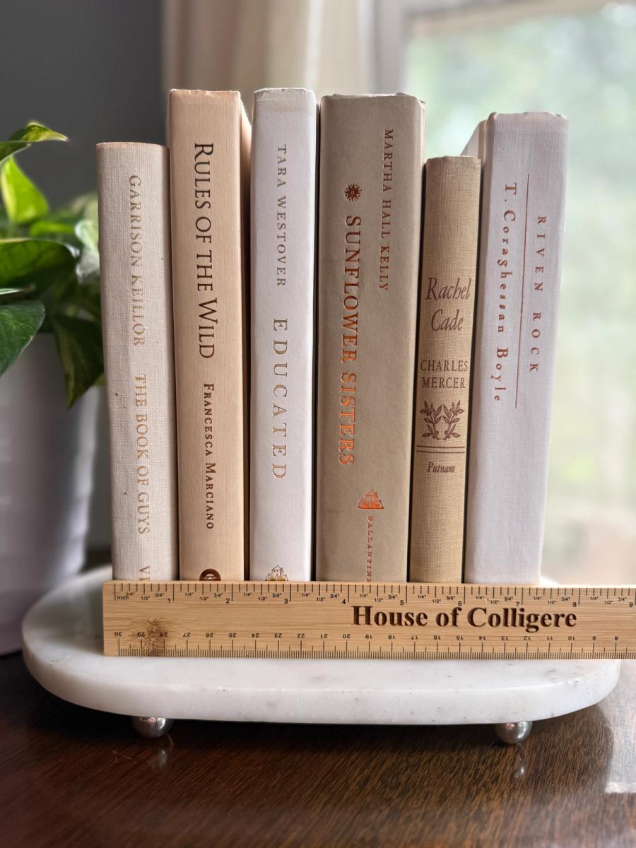 Curated decorative book collection in soft linen-inspired neutrals, featuring ivory, cream, warm beige, and pale taupe clothbound hardcovers with subtle gold, brown, and muted typography.
