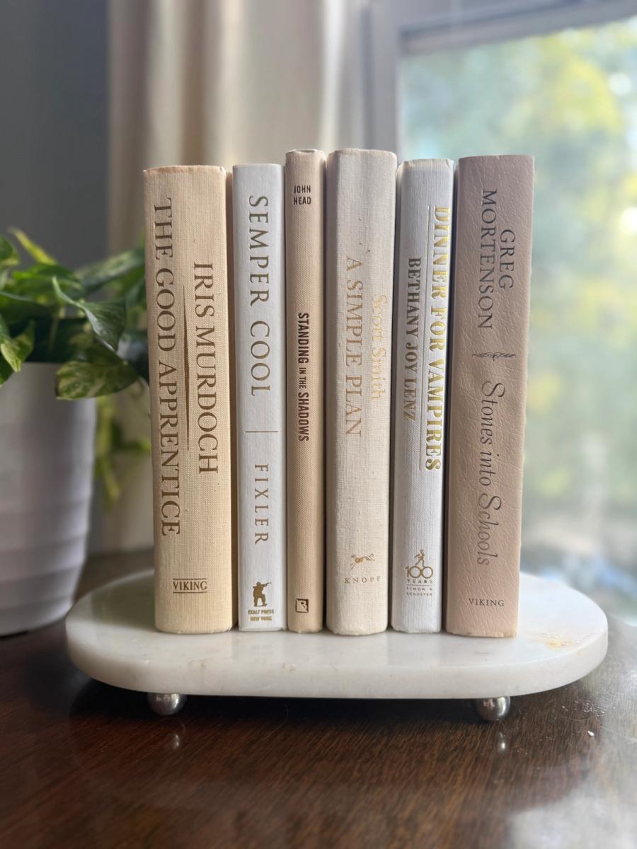 Curated collection of white, ivory, and cream hardcover books with soft neutral tones on a coffee table beside a plant 