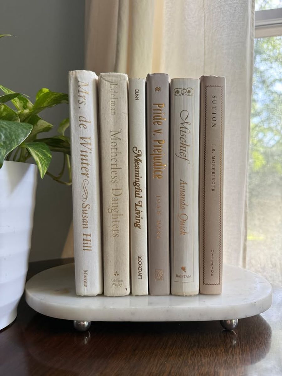 Curated collection of white, ivory, and cream hardcover books with soft neutral tones on a coffee table beside a plant 
