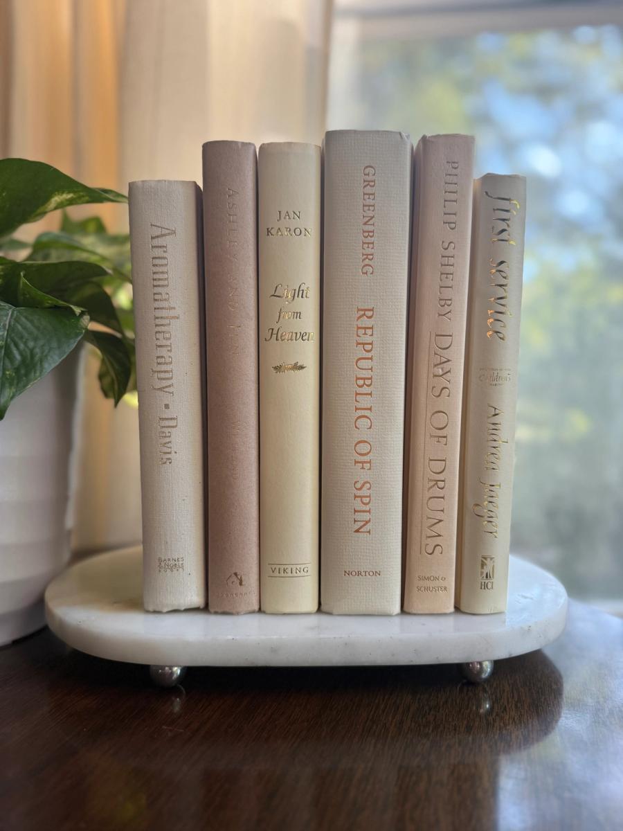 Curated collection of white, ivory, and cream hardcover books with soft neutral tones on a coffee table beside a plant