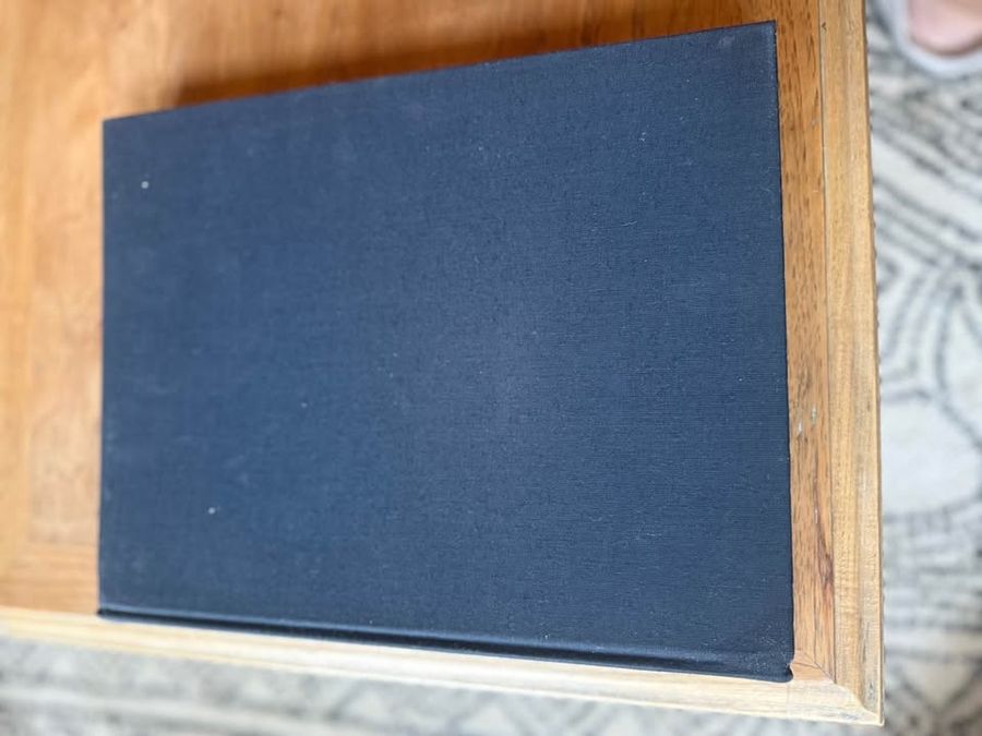 Curated pair of oversized black hardcover books with deep charcoal-black covers, warm aged page edges, and understated gold and cream lettering.