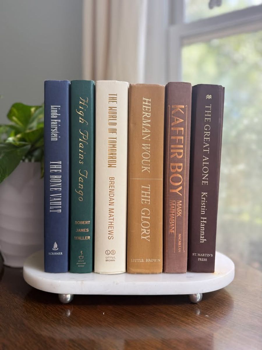Curated collection of rich brown, hunter green, deep navy, and warm ivory books with classic gold accents.