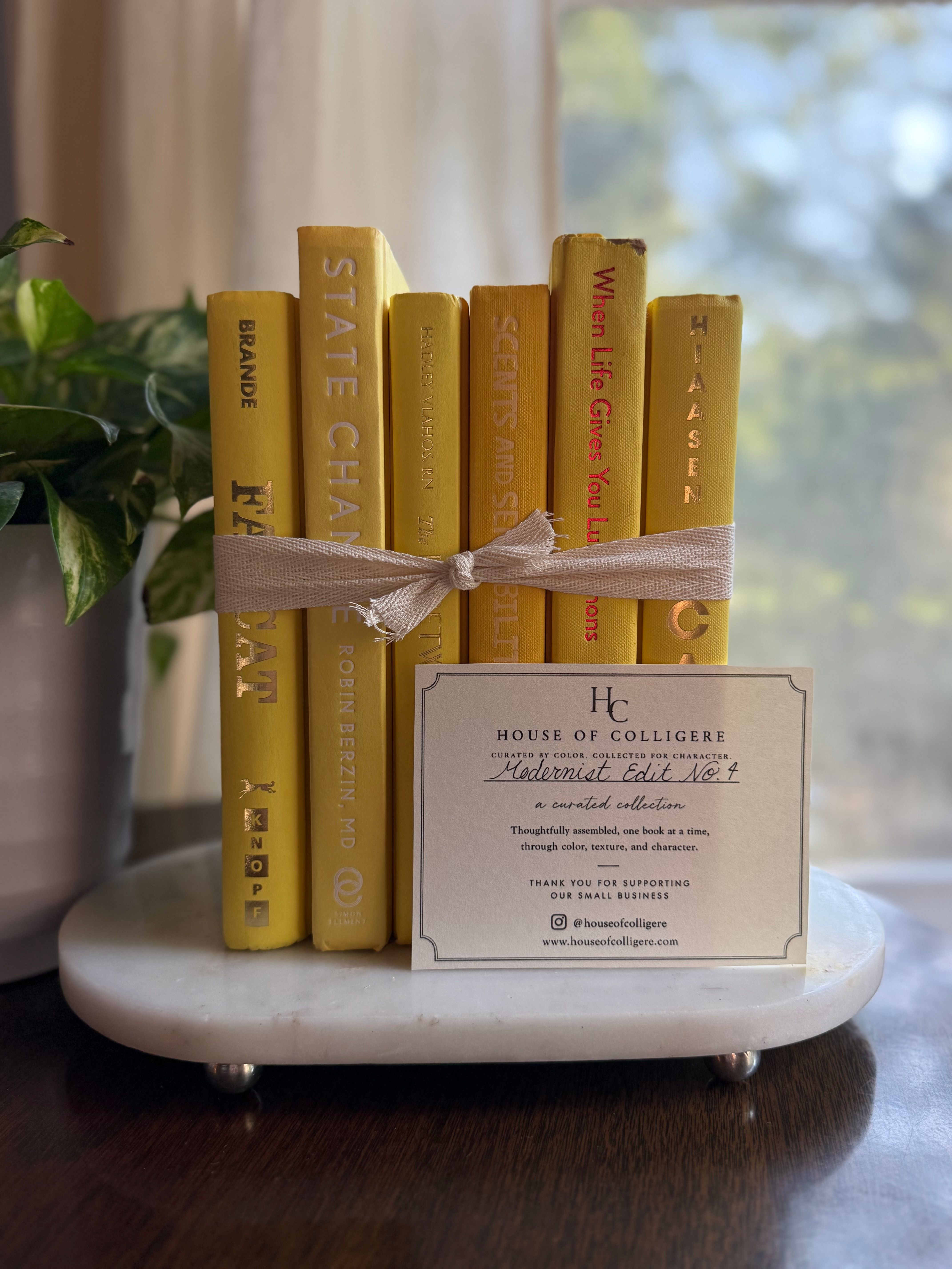 Curated collection of six mustard and golden yellow hardcover books tied with natural cotton ribbon, styled on a marble tray with a House of Colligere Modernist Edit No. 4 collection card.