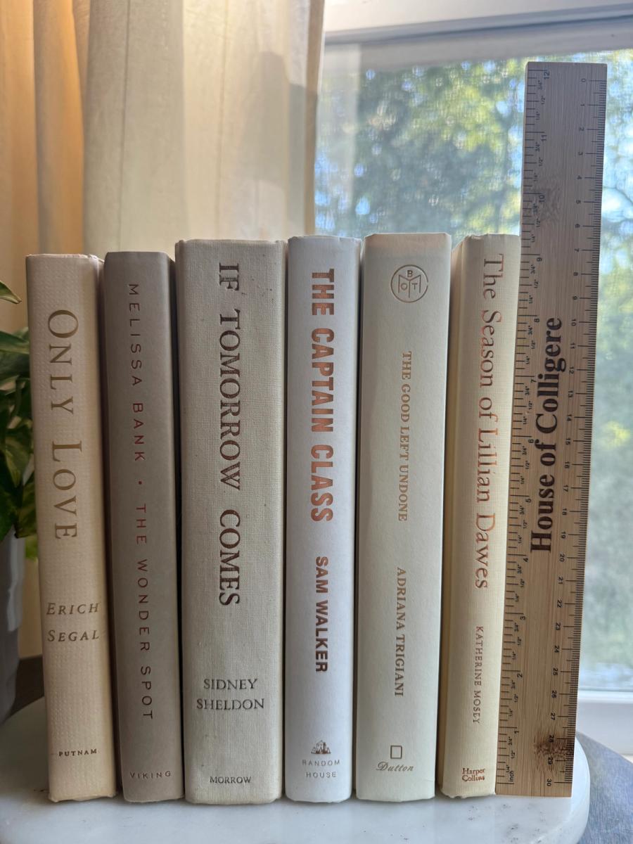 Curated collection of white, ivory, and cream hardcover books with soft neutral tones on a coffee table beside a plant