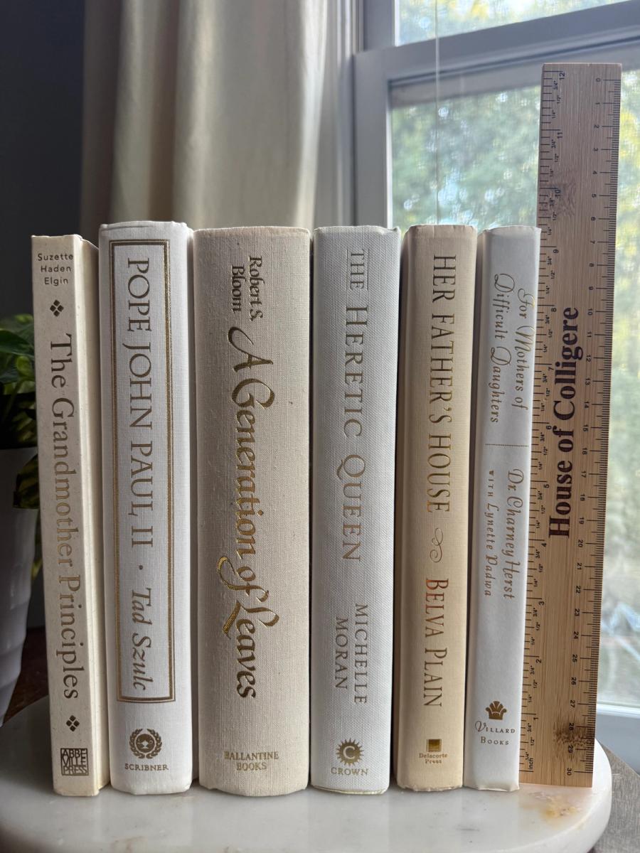Curated collection of white, ivory, and cream hardcover books with soft neutral tones on a coffee table beside a plant
