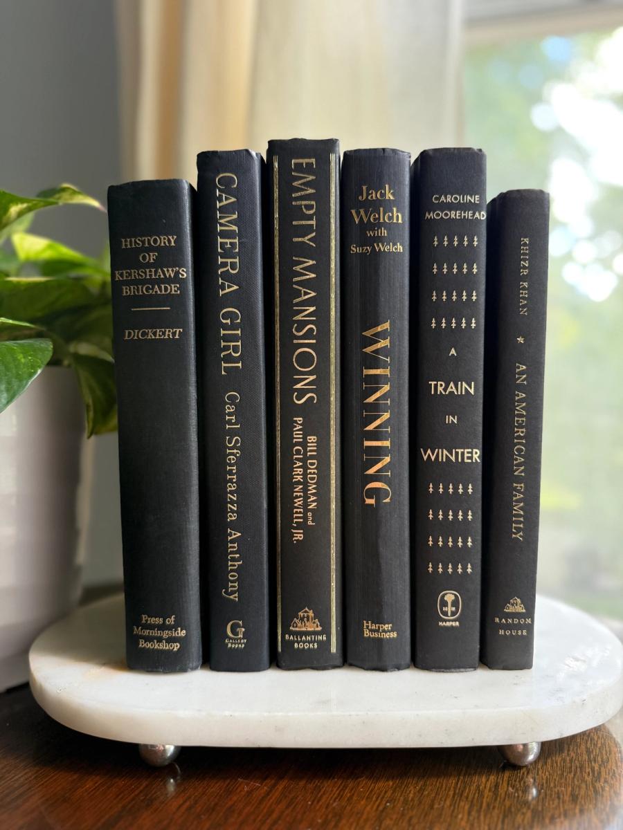 Curated collection of rich charcoal and black books with warm gold lettering and dramatic tonal depth.