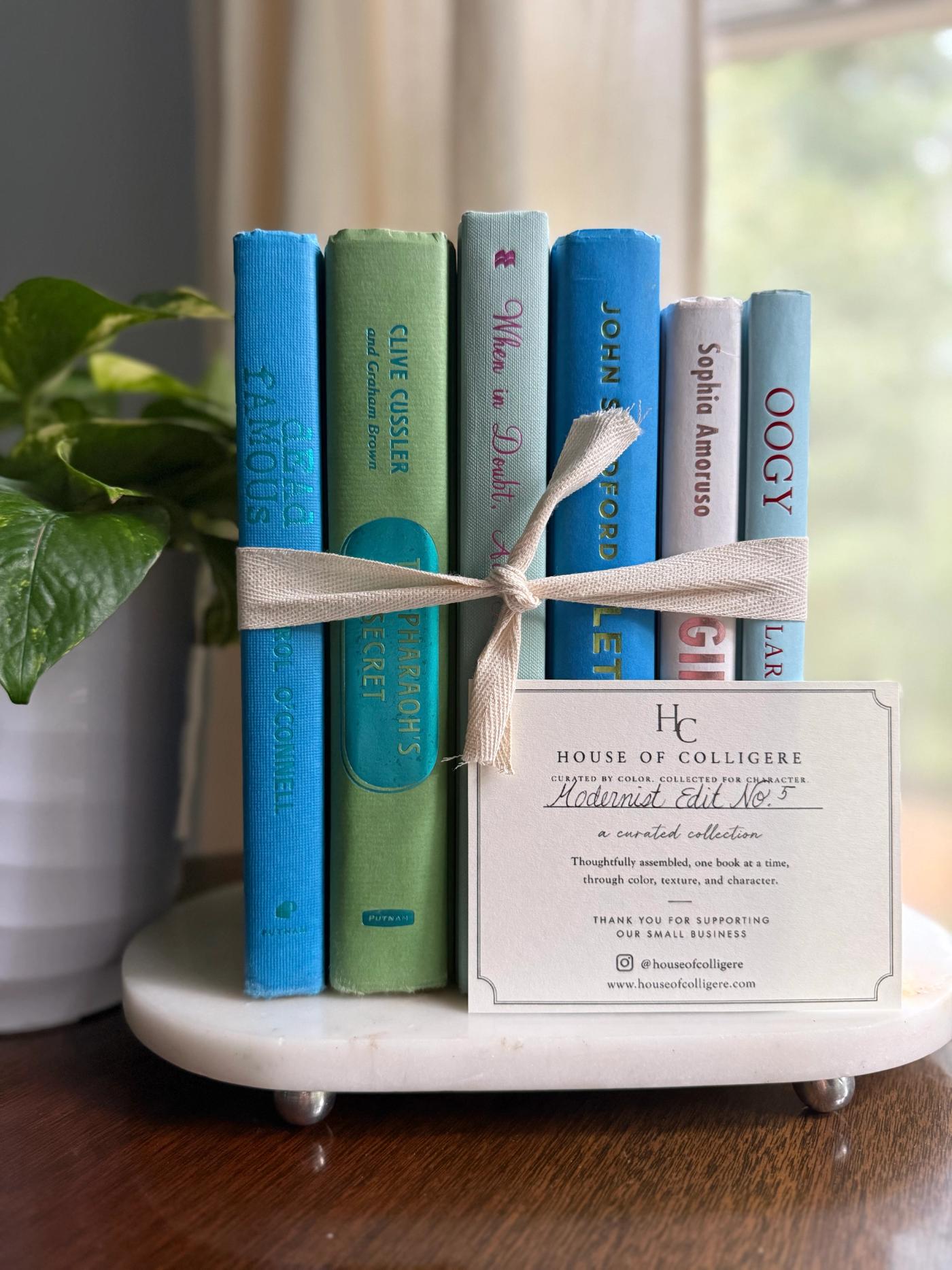 Curated collection of six hardcover books in cobalt blue, sage green, pale aqua, and soft white, tied with natural cotton ribbon and styled beside a House of Colligere collection card.