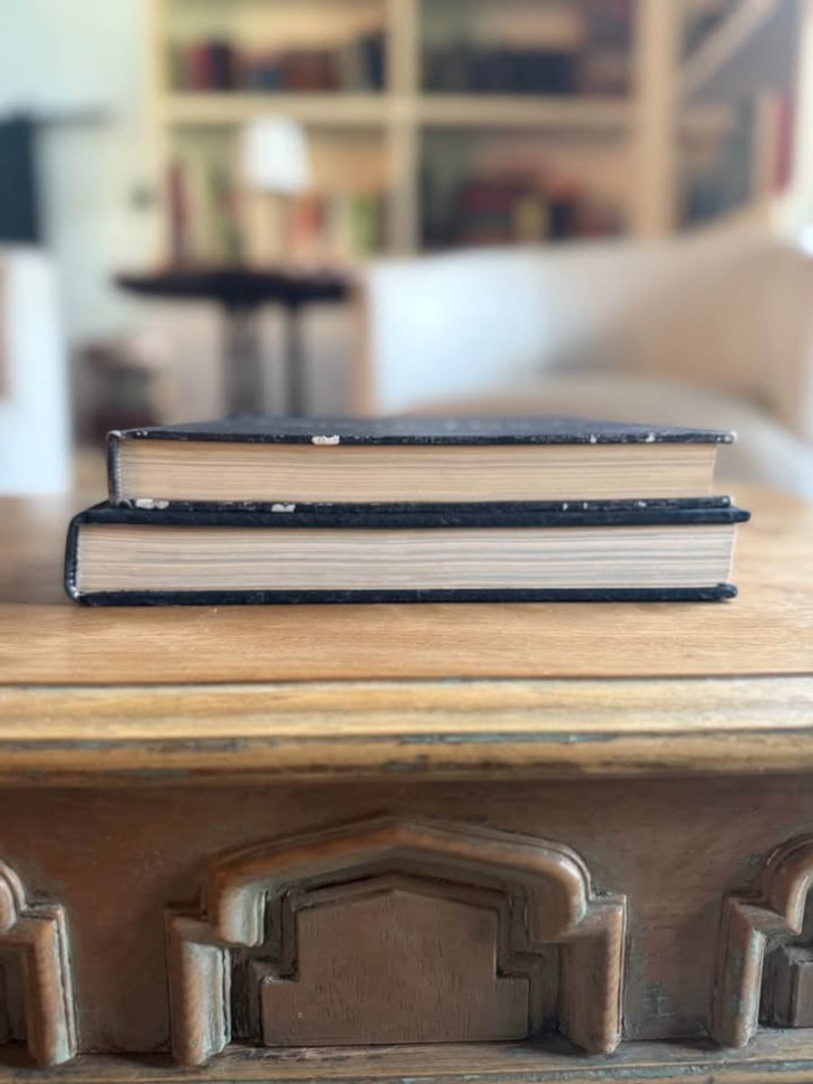 Curated pair of oversized black hardcover books with deep charcoal-black covers, warm aged page edges, and understated gold and cream lettering.