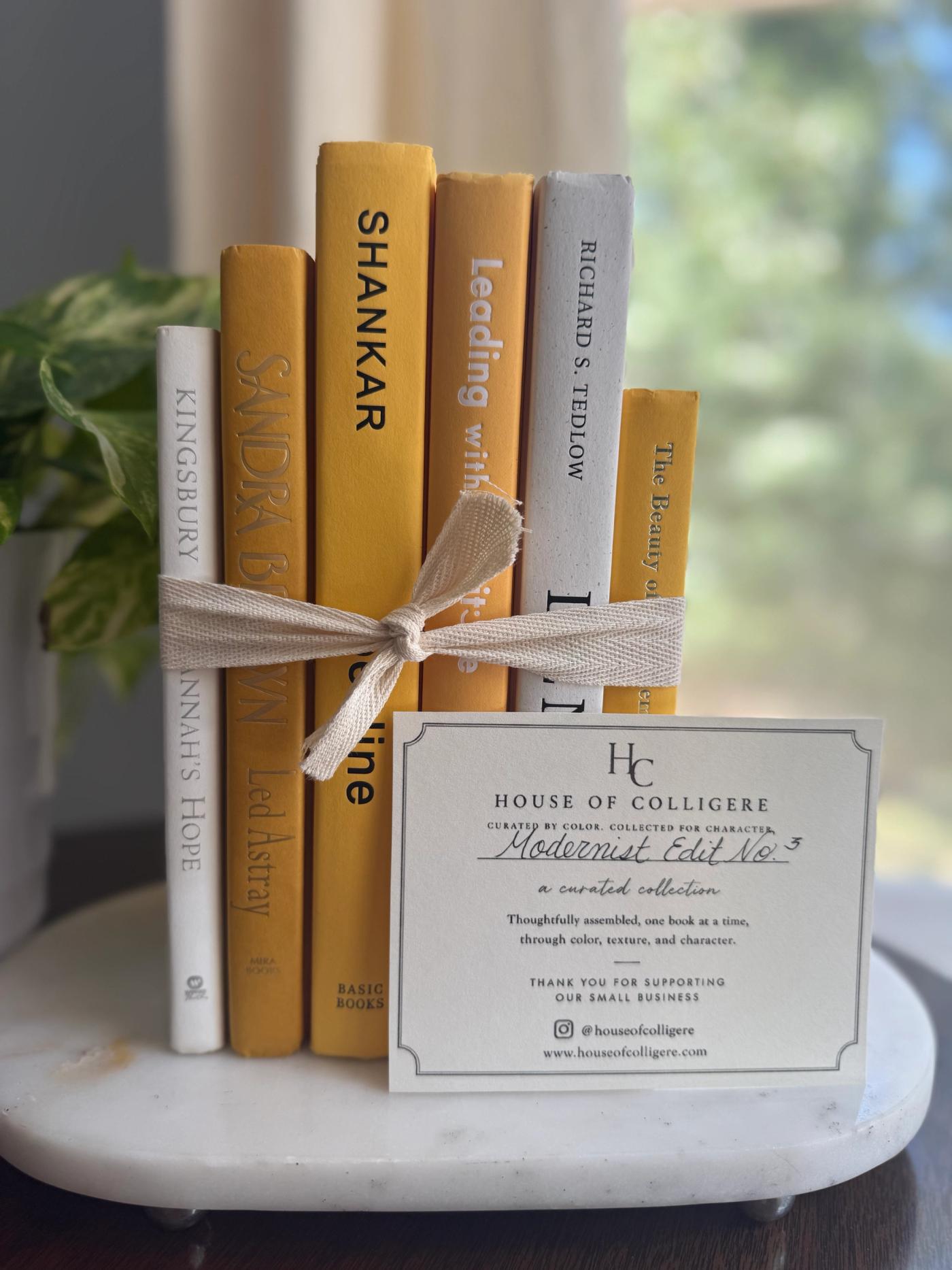 Six curated hardcover books in mustard yellow, golden ochre, cream, and soft white tones, tied with natural linen ribbon and displayed with a House of Colligere Modernist Edit No. 5 card.