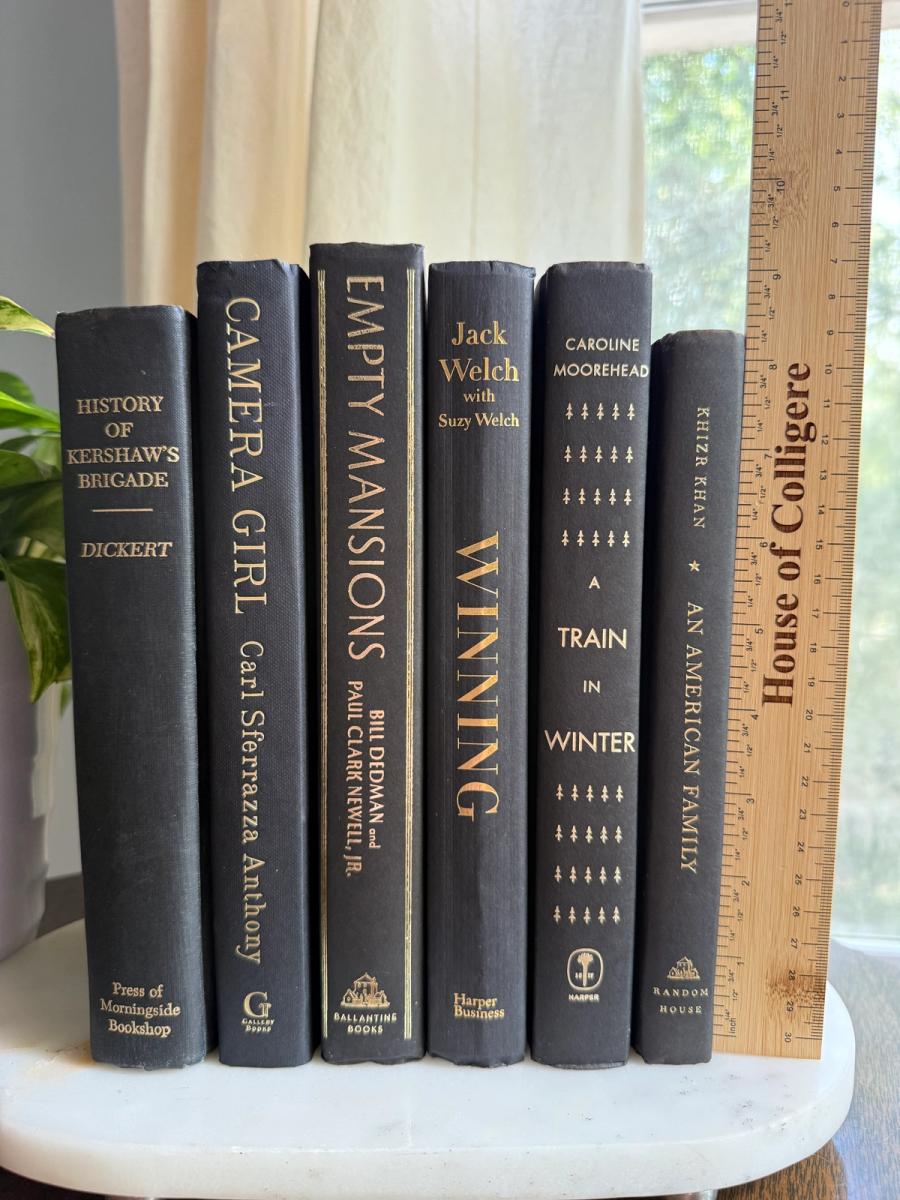 Curated collection of rich charcoal and black books with warm gold lettering and dramatic tonal depth.