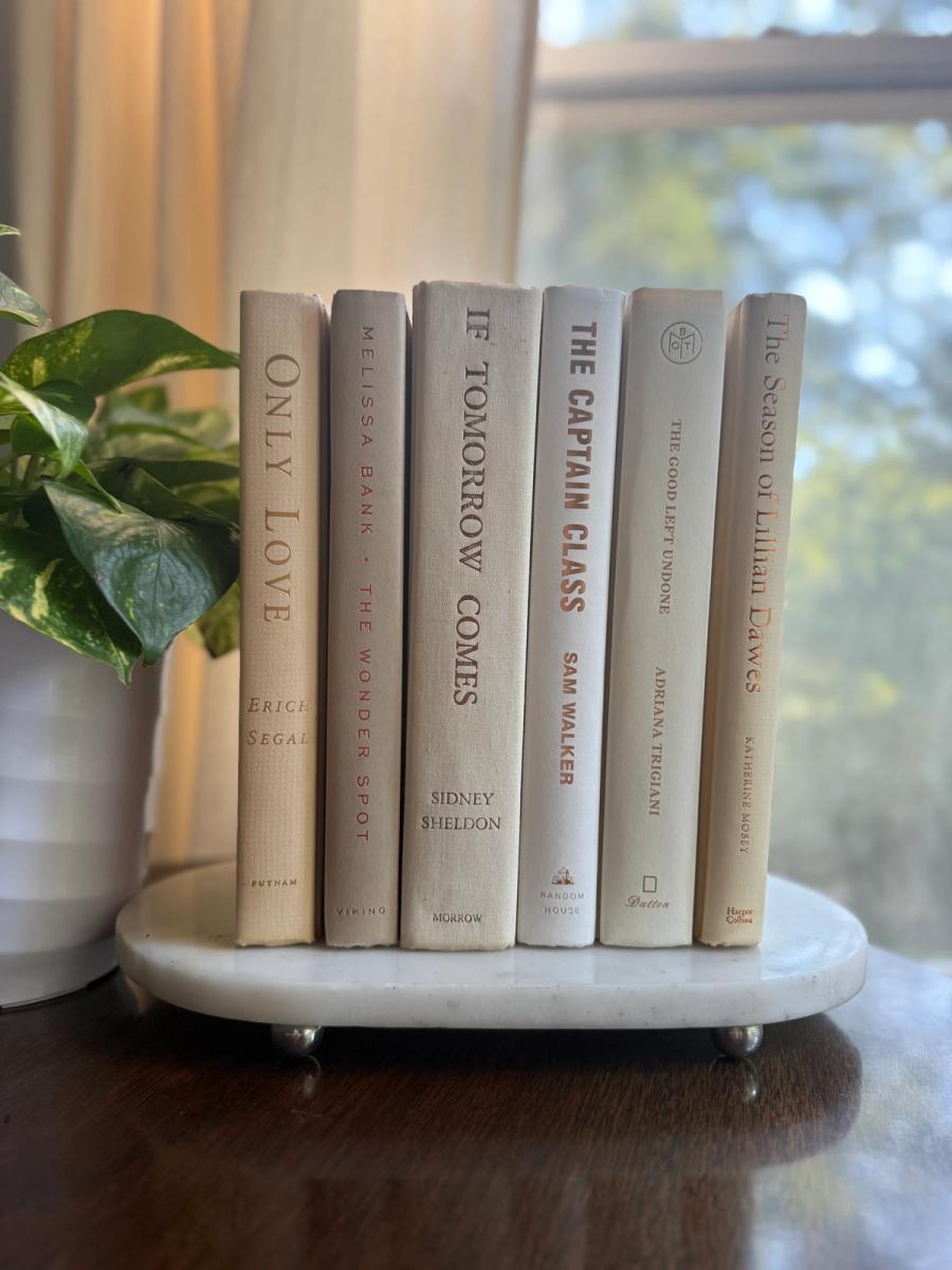 Curated collection of white, ivory, and cream hardcover books with soft neutral tones on a coffee table beside a plant