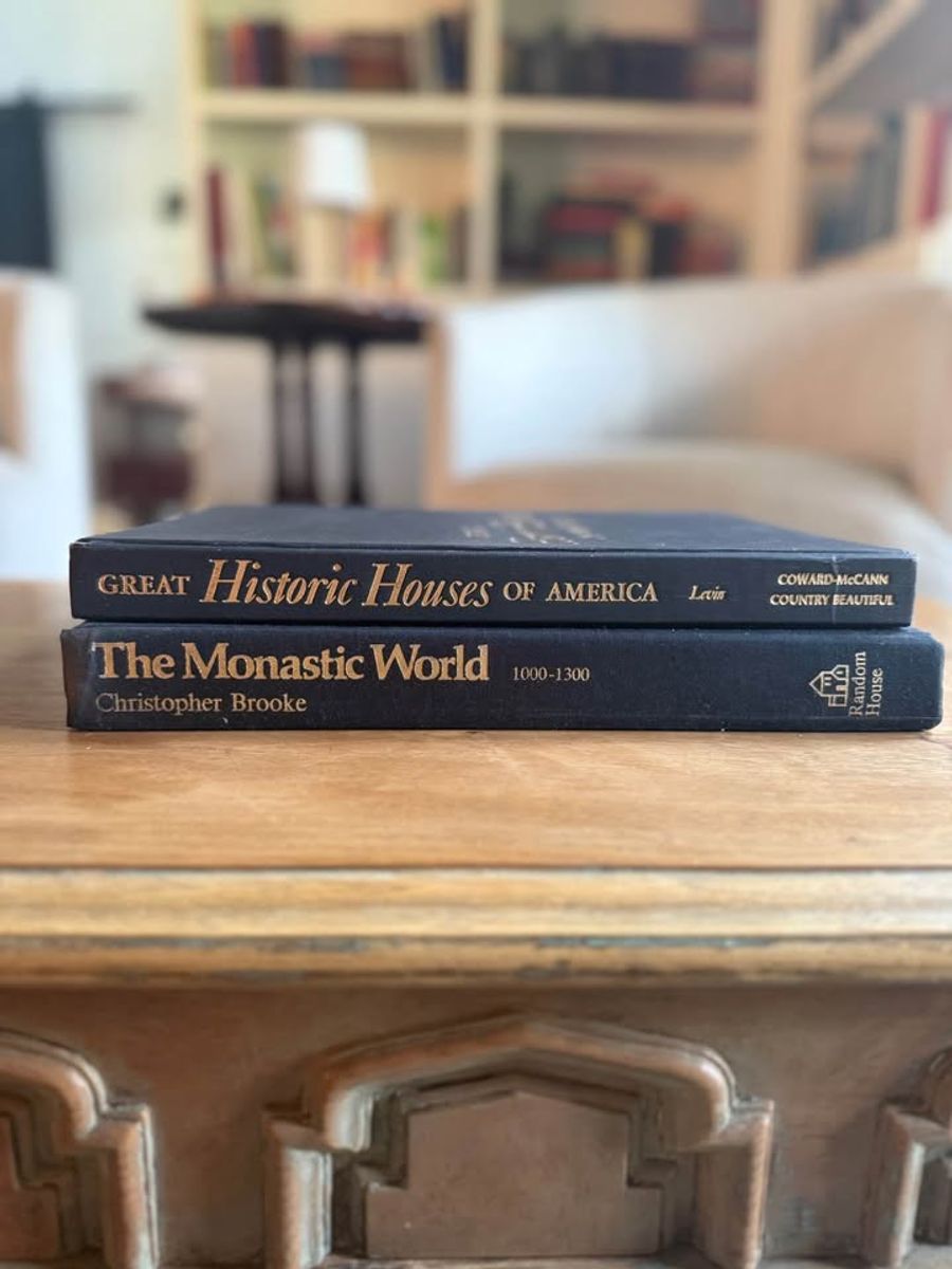 Curated pair of oversized black hardcover books with deep charcoal-black covers, warm aged page edges, and understated gold and cream lettering.