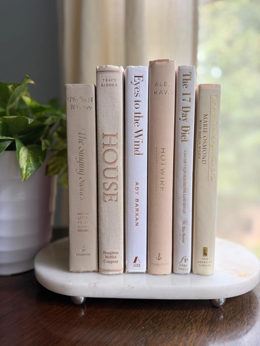 Six white, ivory, and pale taupe hardcover books tied with natural ribbon on a marble tray, with gold-toned lettering and a Linen No. 10 card.