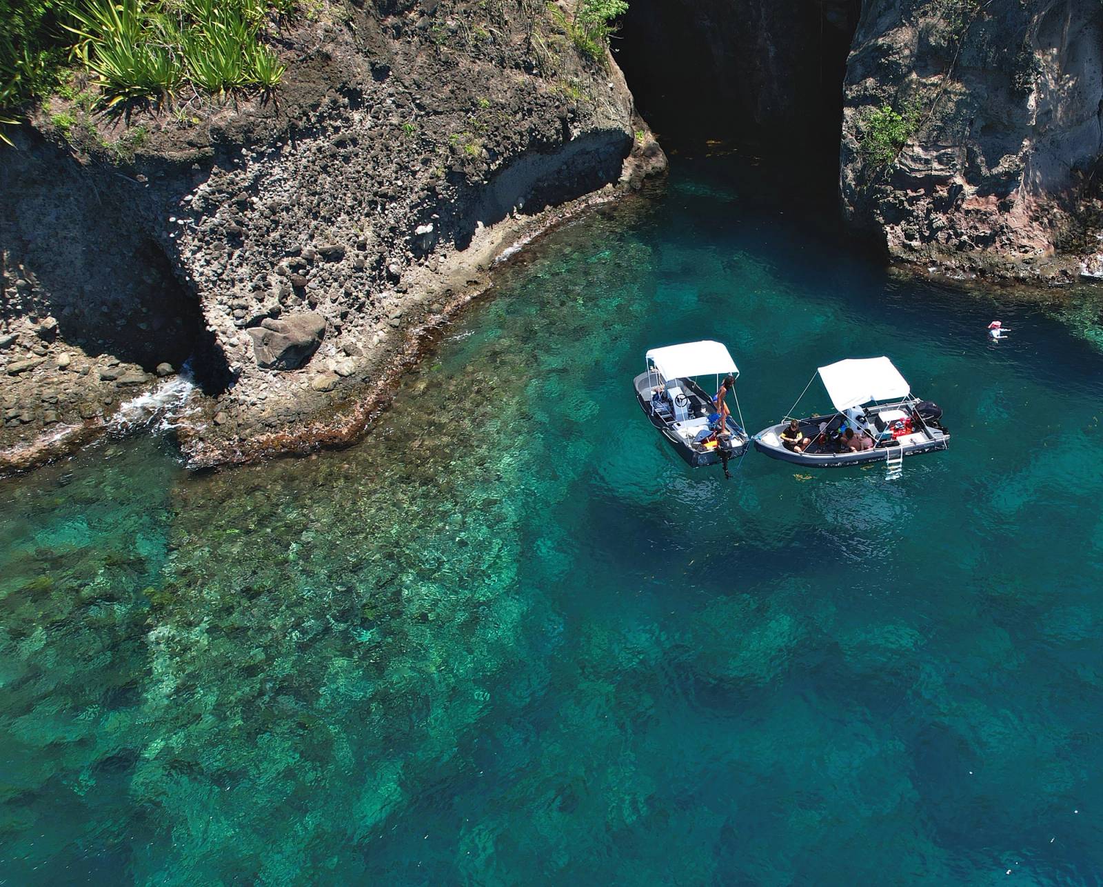 Deux bateaux Ride & Sea au mouillage devant une grotte marine, eau turquoise transparente, vue de drone