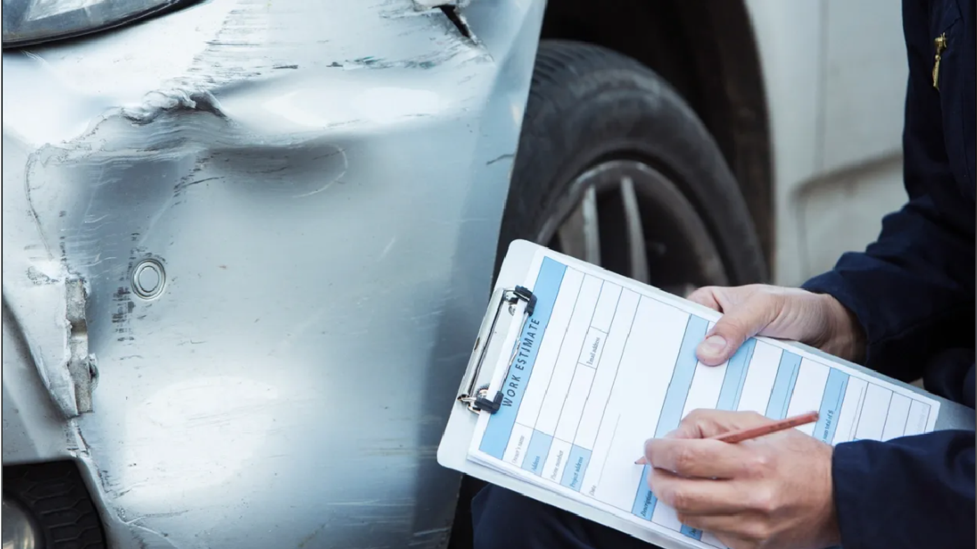 Auto body technician writing a work estimate on a clipboard next to a damaged silver car fender in Austin, TX