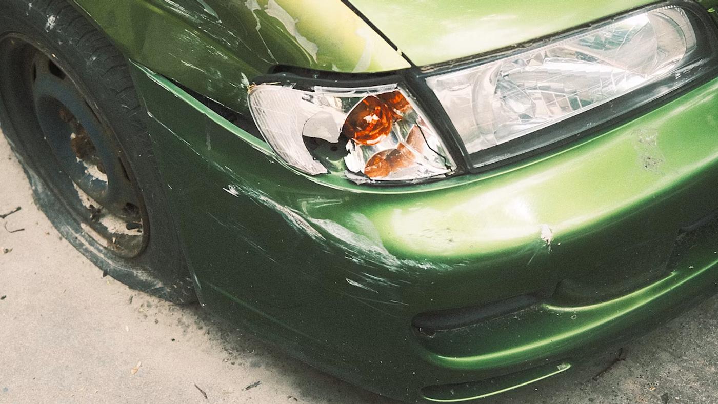 Green car with a dented front bumper in an Austin parking lot — the type of minor damage where filing an insurance claim may not be worth it