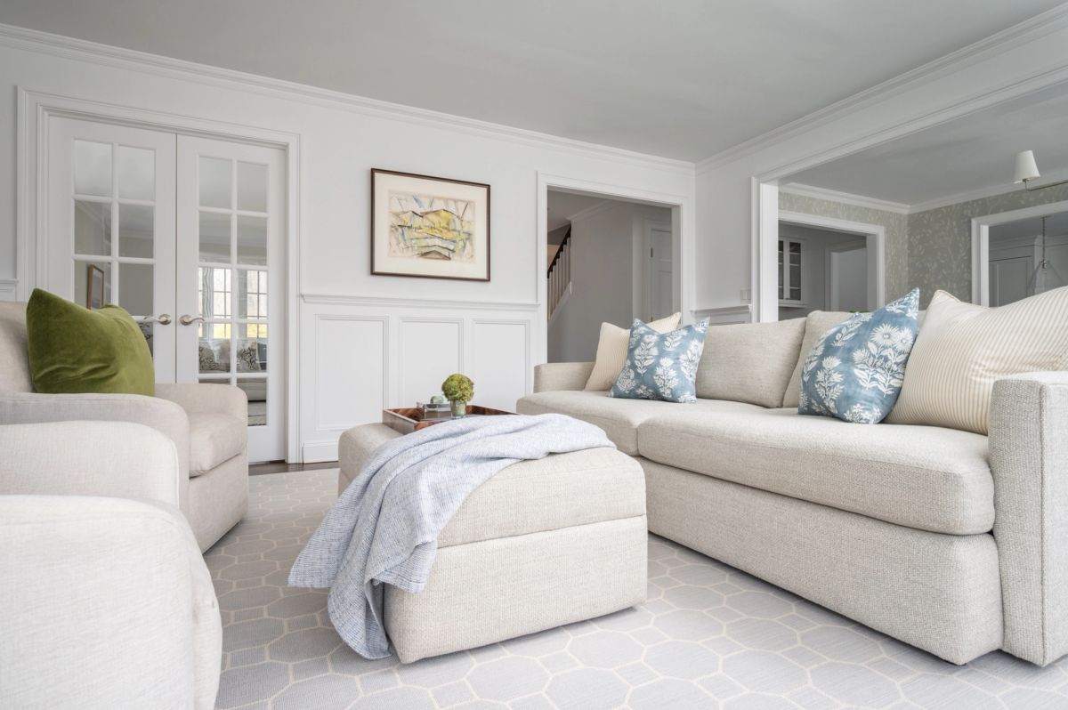 Airy, neutral Darien living room with a linen slipcovered sectional and cream swivel chairs in olive velvet, around a black-marble fireplace flanked by white built-ins.