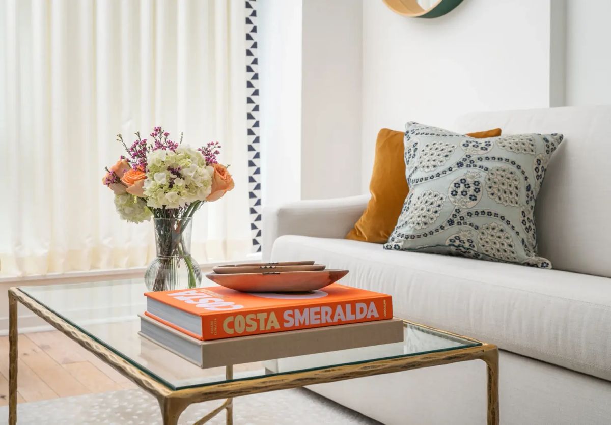 Gramercy Park living room with a gold-leaf glass coffee table styled with roses and hydrangeas, beside a linen sofa with ochre velvet and block-print pillows