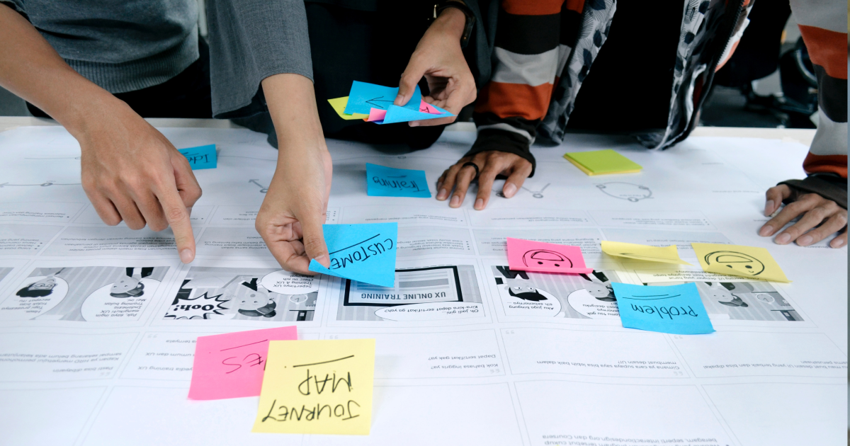 Hands laying out brightly colored sticky notes with product discovery steps written on them.