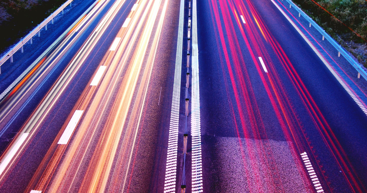Time-lapse photo of traffic on highway at night, showing car lights as colorful streaks.