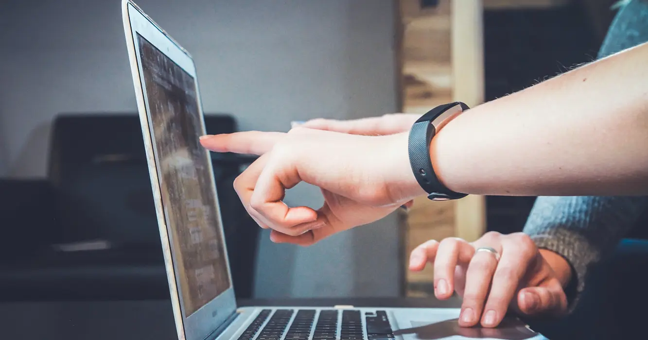 Close-up of hand pointing to screen of open laptop while another person works the track pad.