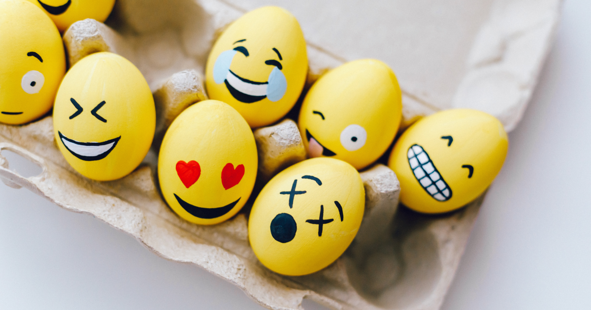 Carton of eggs decorated to look like different smiley face emojis.