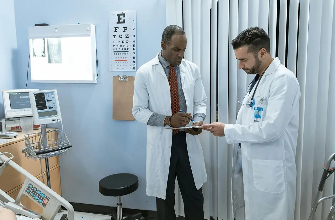 Two physicians in white lab coats standing in hospital room conferring over patient chart.