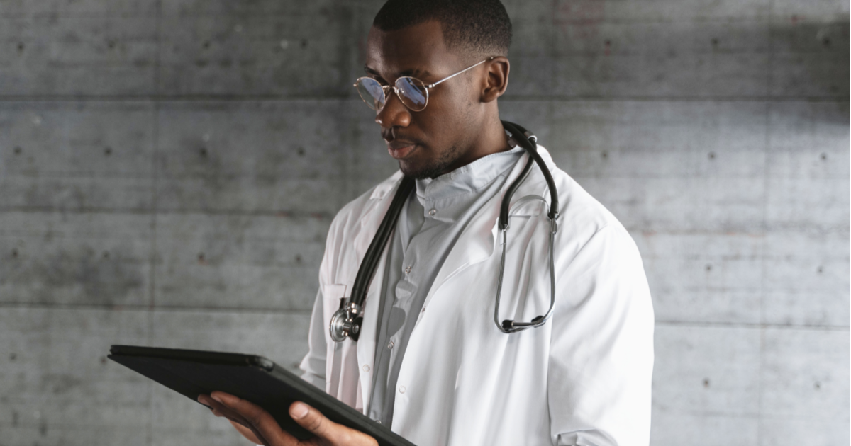 Doctor in white lab coat and stethoscope working on tablet device.