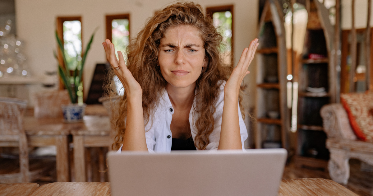 Woman sitting in front of open laptop looking at screen with exasperated expression.