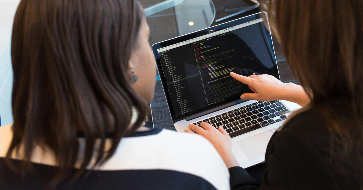 Two app developers discussing code displayed on an open laptop.