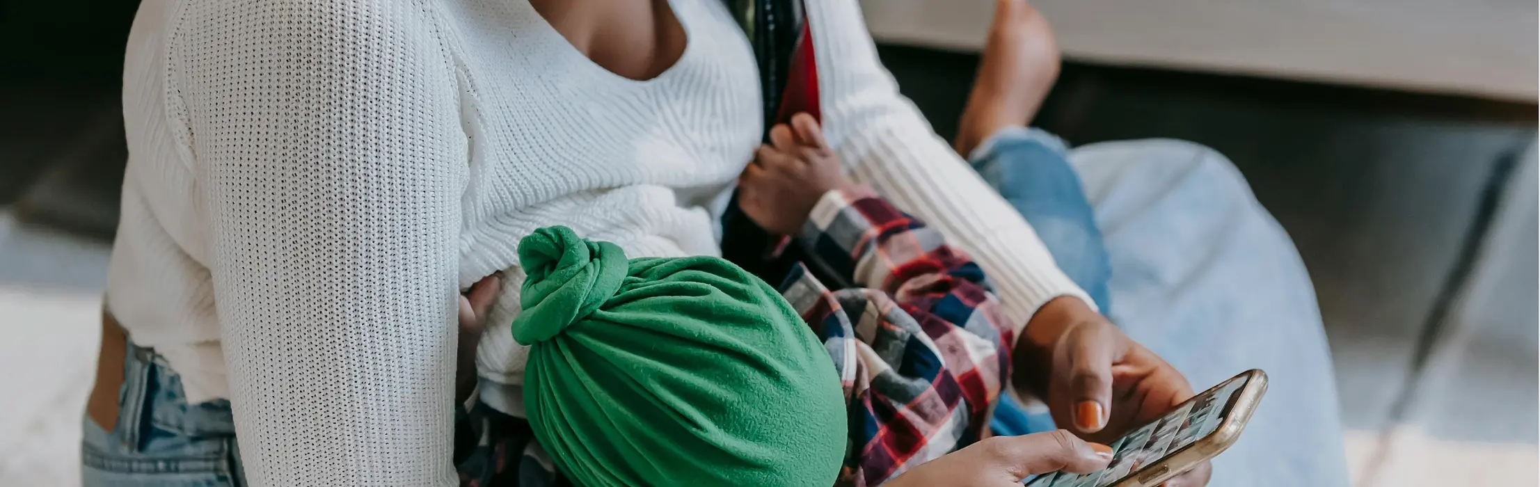 Mother sitting on living room floor nursing young baby while working on her smartphone.