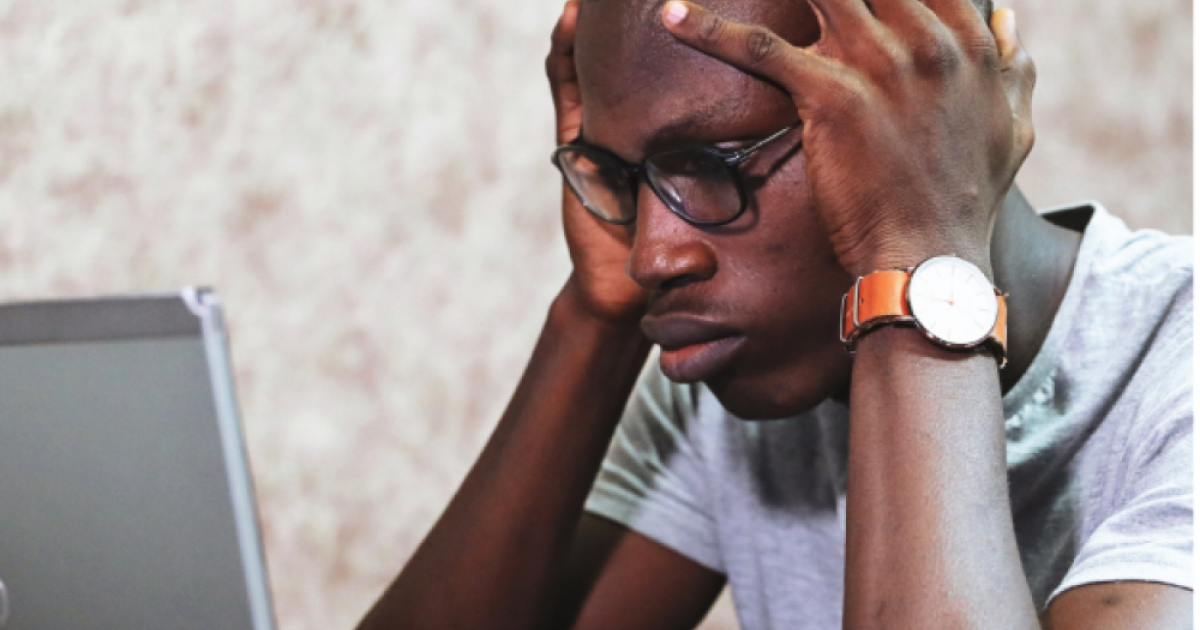 Young man wearing glasses and watch staring at laptop screen with hands on his head in frustration