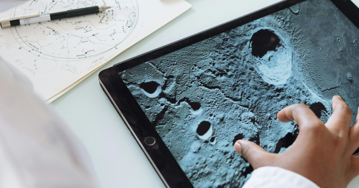 Elementary school student using tablet device displaying images of a planet or moon surface.