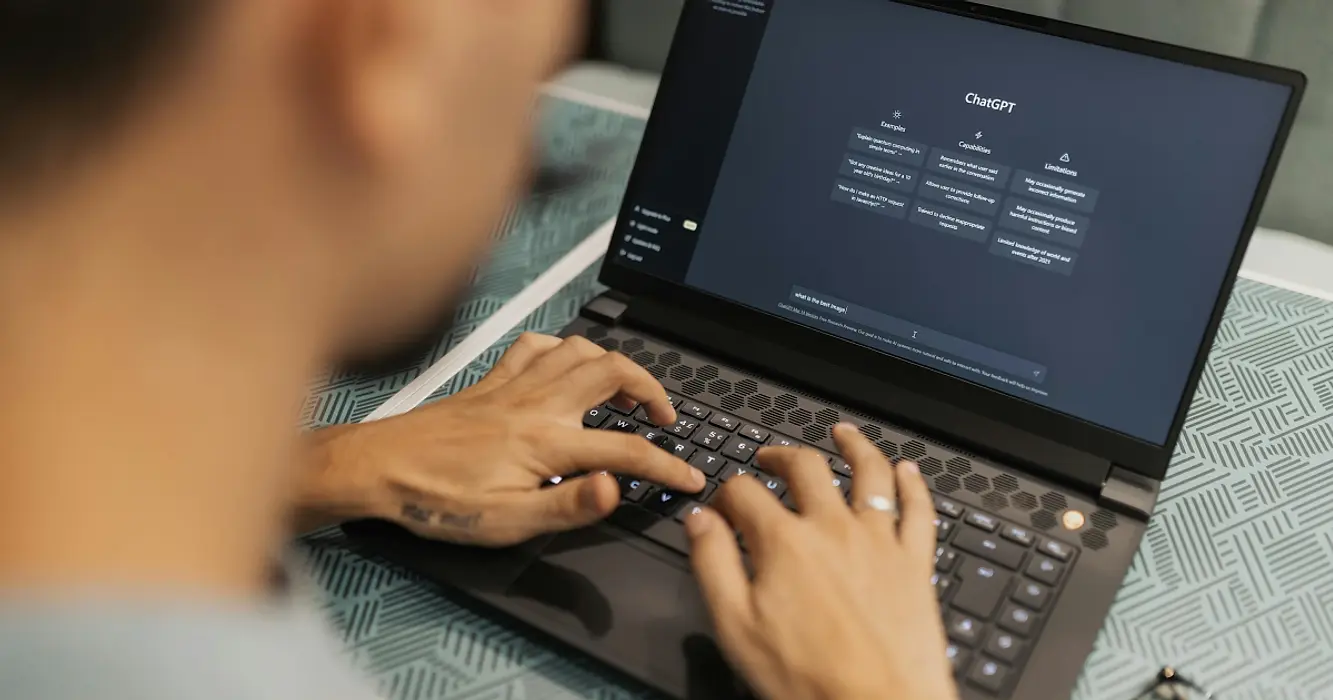 Over-shoulder view of person typing on a laptop displaying the prompt screen for ChatGPT