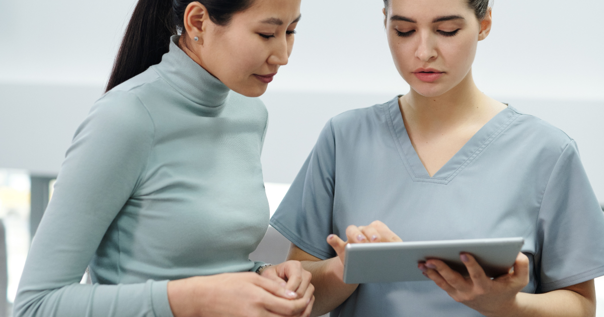 Healthcare worker in scrubs holding tablet device and showing something to patient standing next to her.
