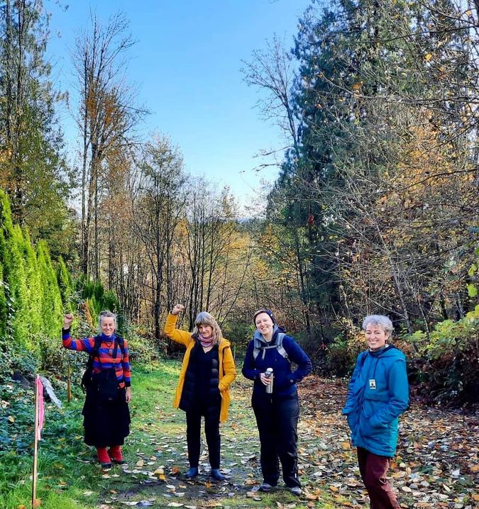 The author and her fellow land defenders smiling and raising their fists in bright clothing in front of a cedar forest