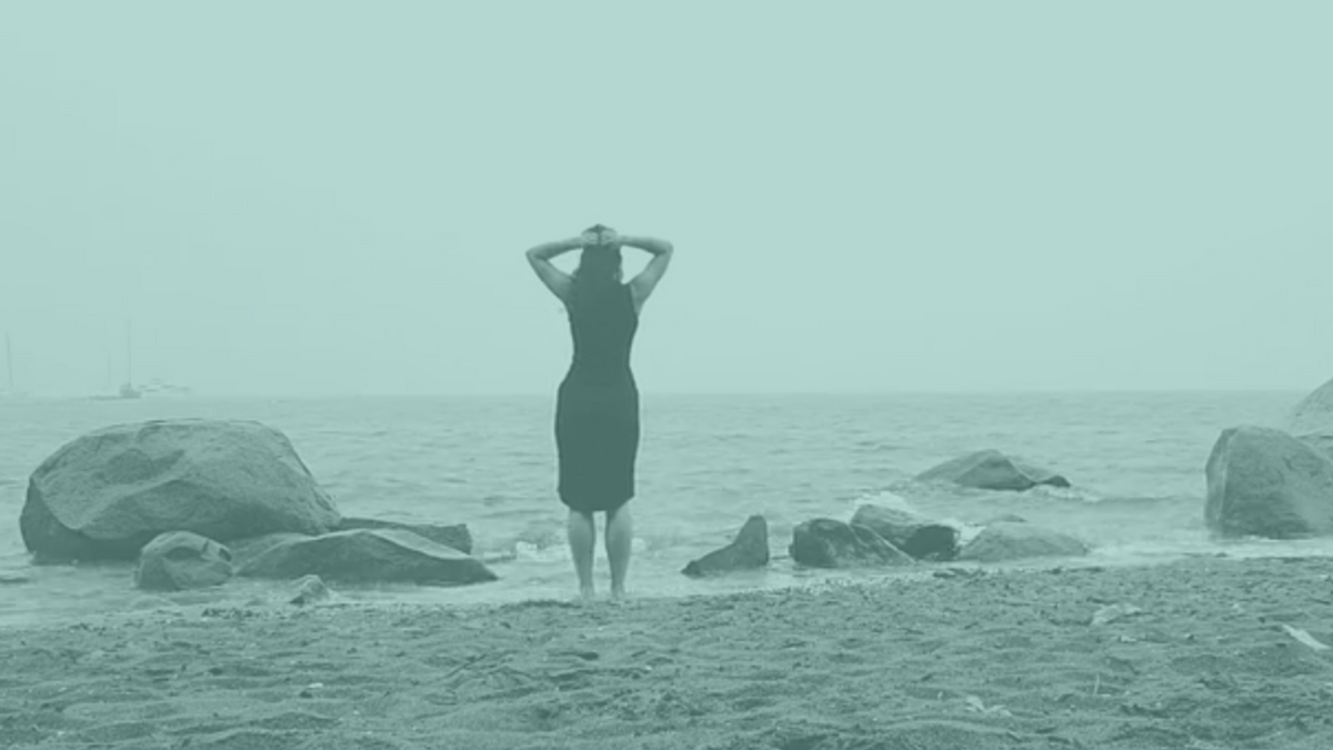 A woman on the beach facing the water with her hands on her head