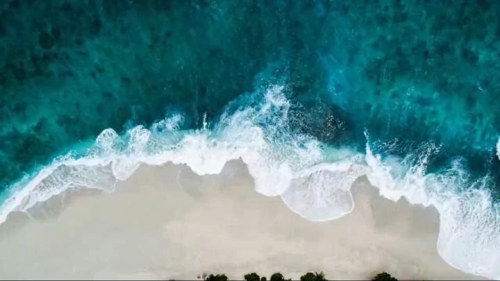Vista aérea de ondas do mar chegando a uma praia de areia clara